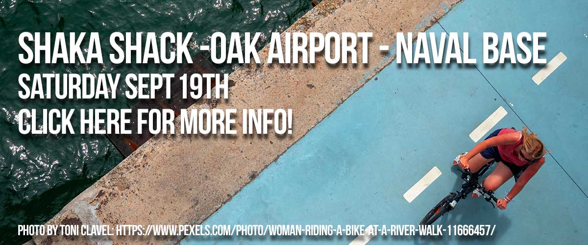 Background bird's eye view of a diagonal image with water on the top left side with the cyclist on the right side on a light blue pavement with white stripes with white type saying Shaka Shack -Oak Airport - Naval Base on the first line and Saturday Sept 19th on the second line and Click for more info! on the third line and Photo by Toni Clavel: https://www.pexels.com/photo/woman-riding-a-bike-at-a-river-walk-11666457 on the fourth line.